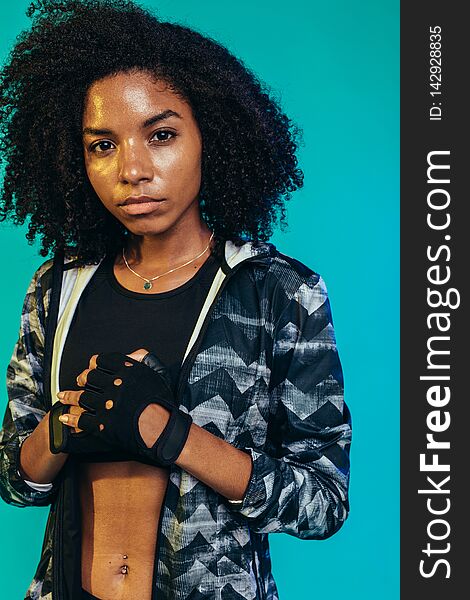 Tough young woman in sportswear standing on blue background. Fit female wearing gloves ready for workout in studio