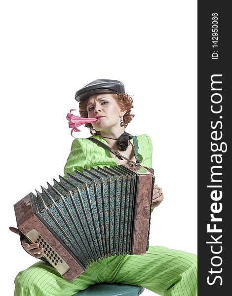 A young woman in a green pantsuit with a cap on her head and a flower in her teeth playing Russian fur accordion. A young woman in a green pantsuit with a cap on her head and a flower in her teeth playing Russian fur accordion