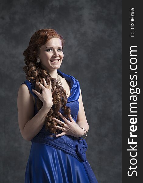 Young woman in a dark blue classic evening dress posing in the studio on a gray background. Young woman in a dark blue classic evening dress posing in the studio on a gray background