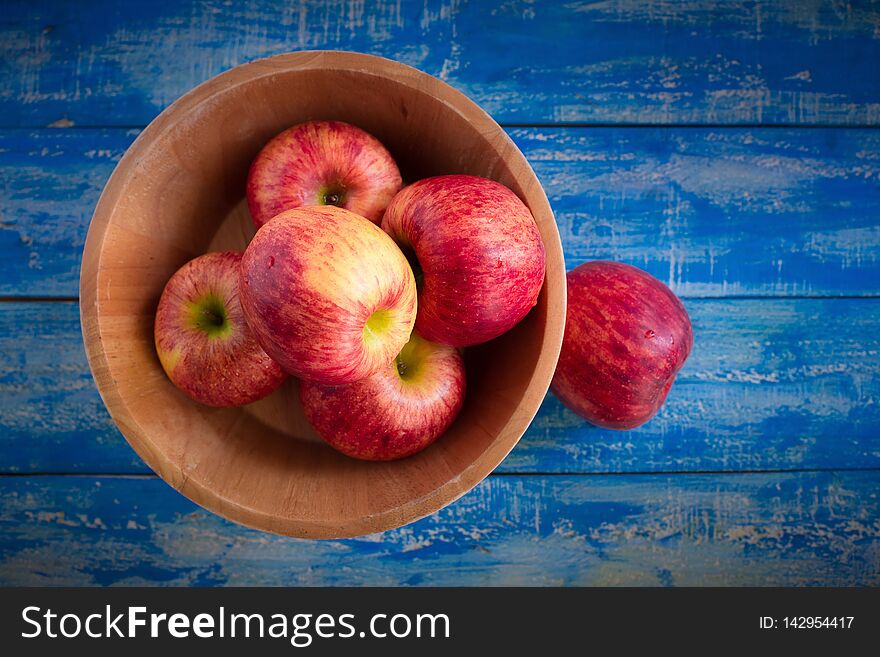 Red apples in a wooden bowl on a blue wooden background