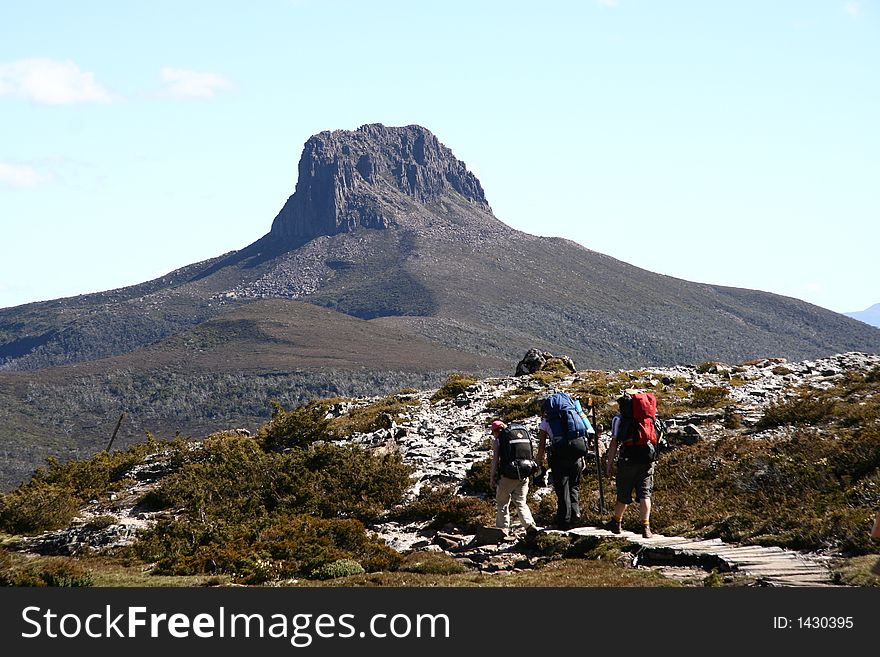 Three hikers walking along a remote track in front of a distant mountain. Three hikers walking along a remote track in front of a distant mountain