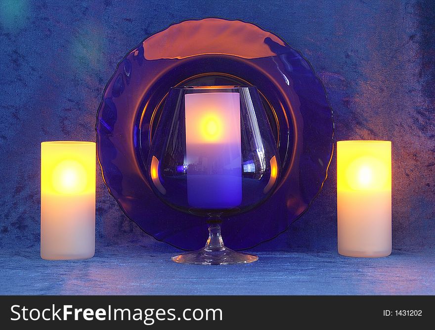Blue Goblet,candles,plate.Blue background. Blue Goblet,candles,plate.Blue background