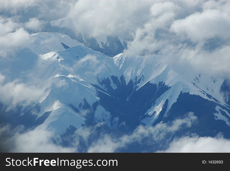Aerial shot of snowy alpine among clouds, snow capped mountains.