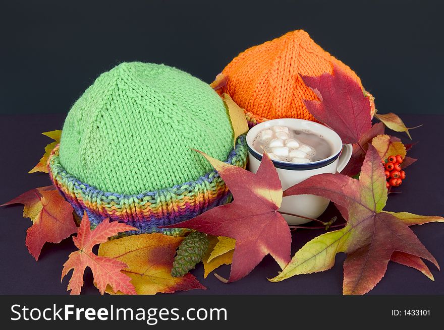 Two stocking caps with fall colored leaves and a cup if hot chocolate