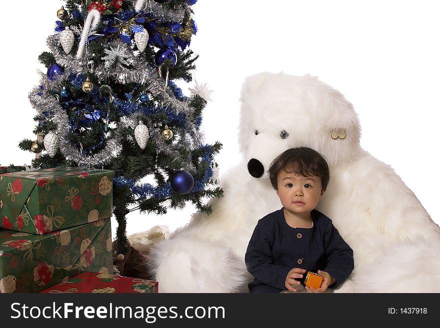 A little boy sits between a giant stuffed bears legs, under the christmas tree. A little boy sits between a giant stuffed bears legs, under the christmas tree