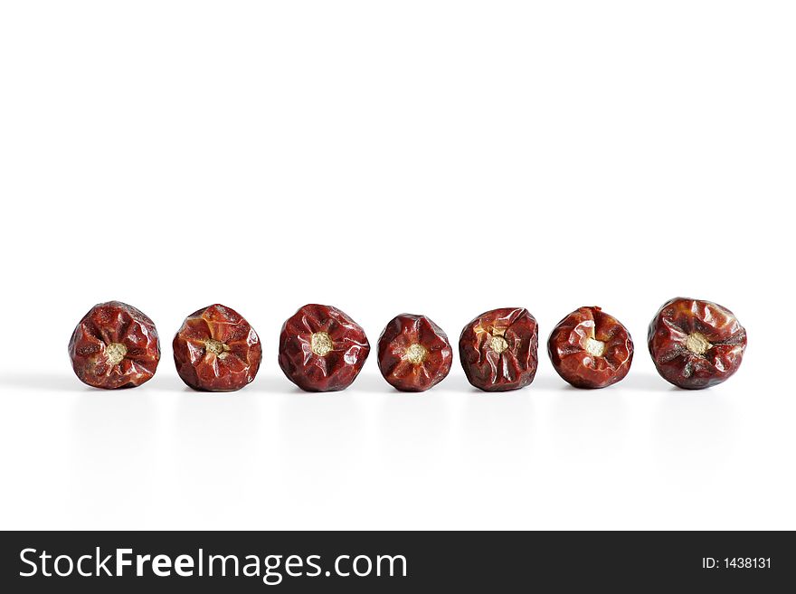 Seven dried chillies in a row isolated against a white background
