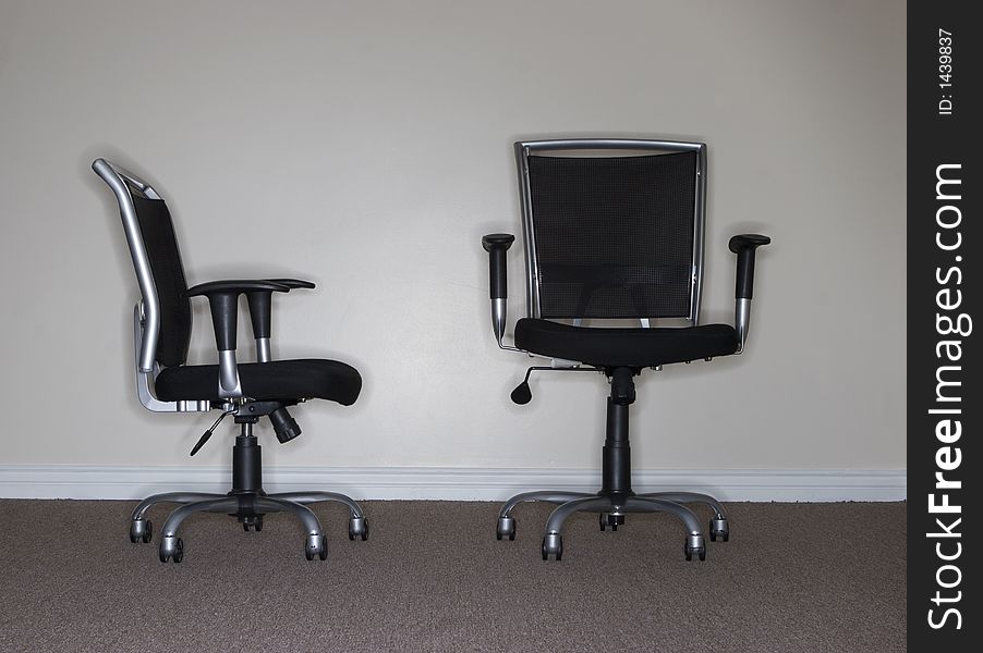 One business chair is facing and looking at the taller, more confident business chair, which is the boss. One business chair is facing and looking at the taller, more confident business chair, which is the boss