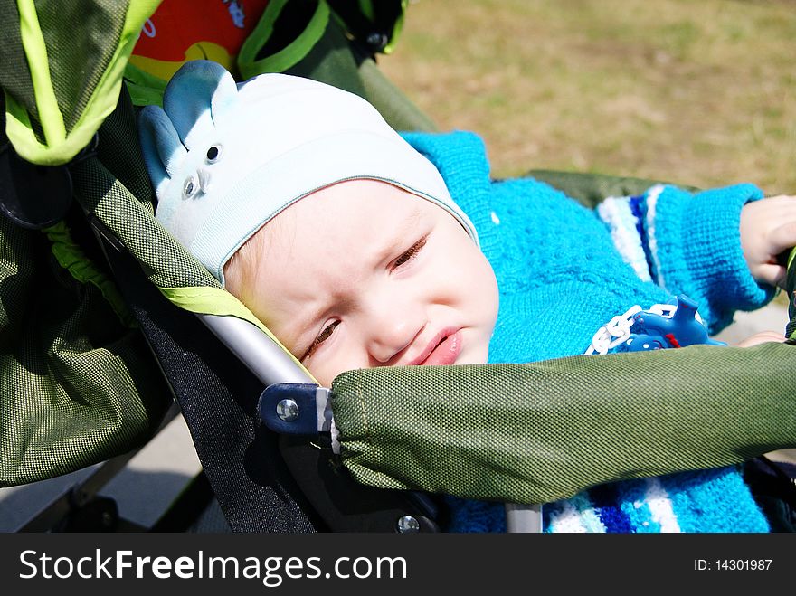 In the summer the small ten-monthly child in a blue suit sits in a green carriage the dissatisfied. In the summer the small ten-monthly child in a blue suit sits in a green carriage the dissatisfied