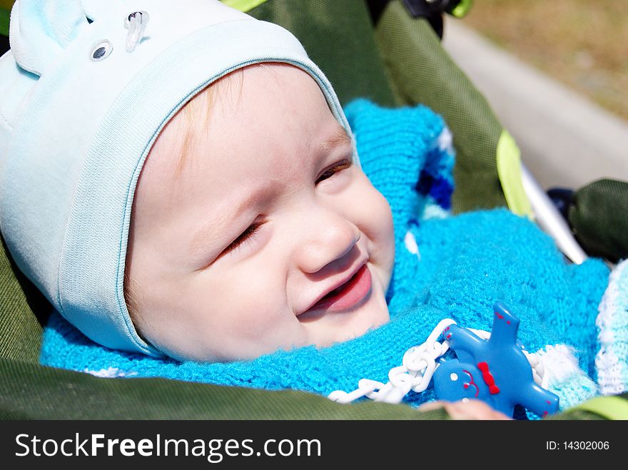 The beautiful smiling small child in a blue suit and a hat sits in a children's carriage and looks aside. The beautiful smiling small child in a blue suit and a hat sits in a children's carriage and looks aside