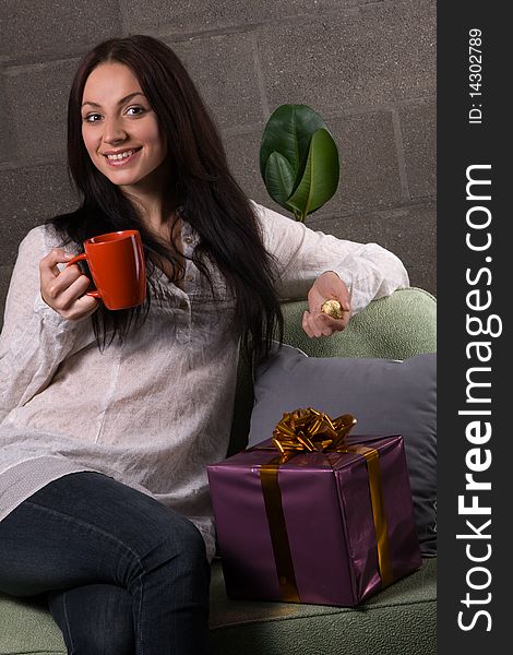 Charming young woman with a gift box, in home interior