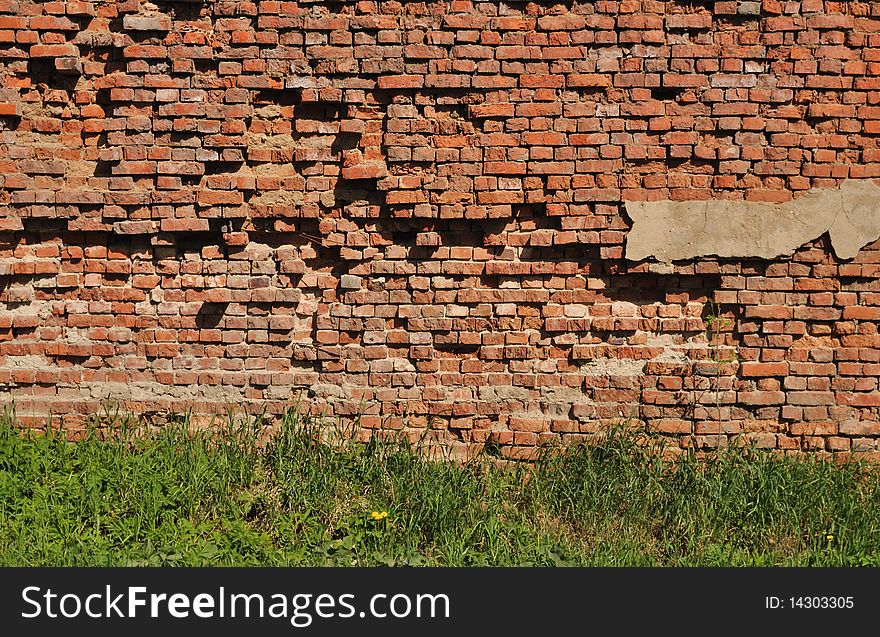 Fragment of old destroyed brick wall background with green grass