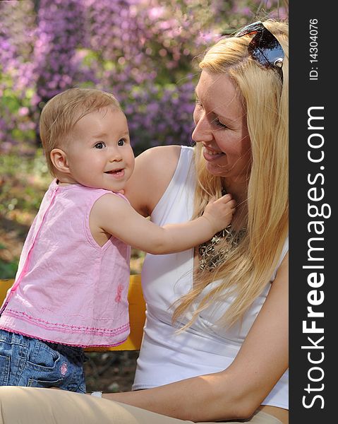 The little girl with mum sit in a garden on a bench in the afternoon