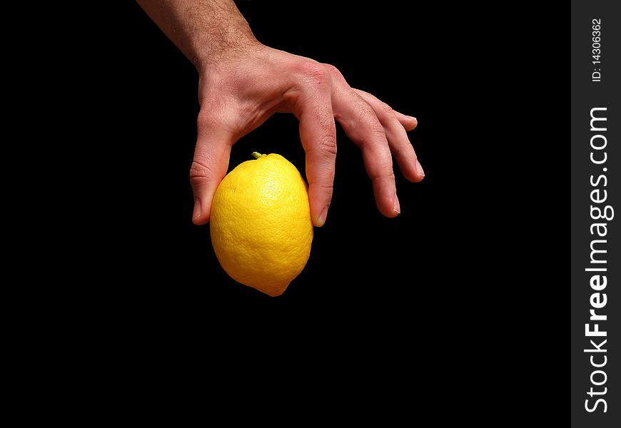 Male hand holding a yellow lemon. On a black background.