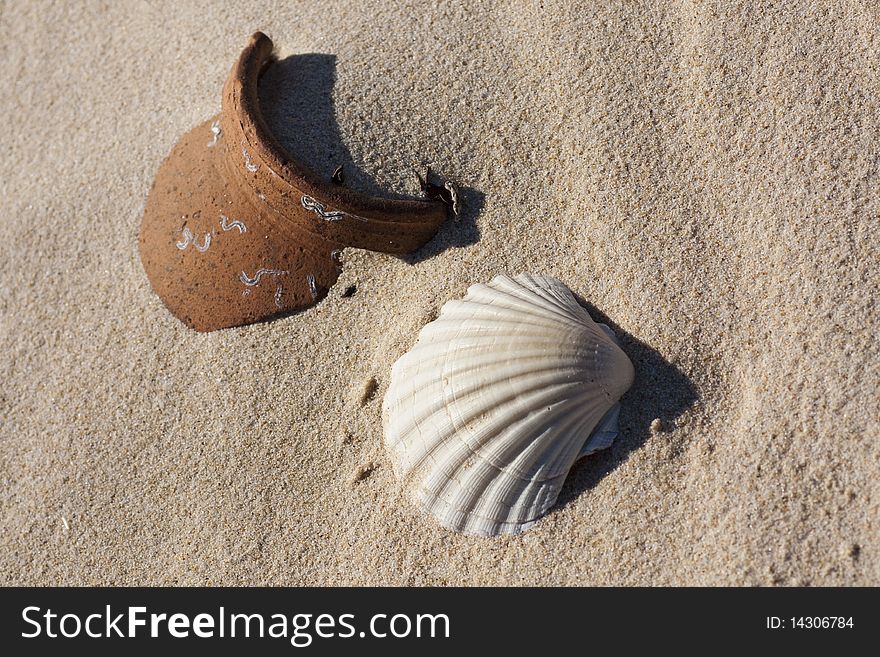 Close up view of an empty shell and a broken ceramic pot buried on the beach sand. Close up view of an empty shell and a broken ceramic pot buried on the beach sand.