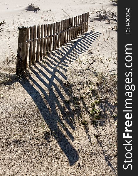 View of a section of a fence buried on the dune sand on the beach. View of a section of a fence buried on the dune sand on the beach.