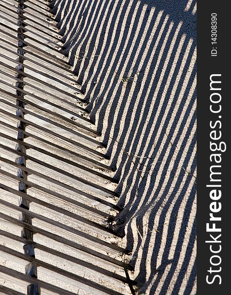 View of a section of a fence buried on the sand making a shadow. View of a section of a fence buried on the sand making a shadow.