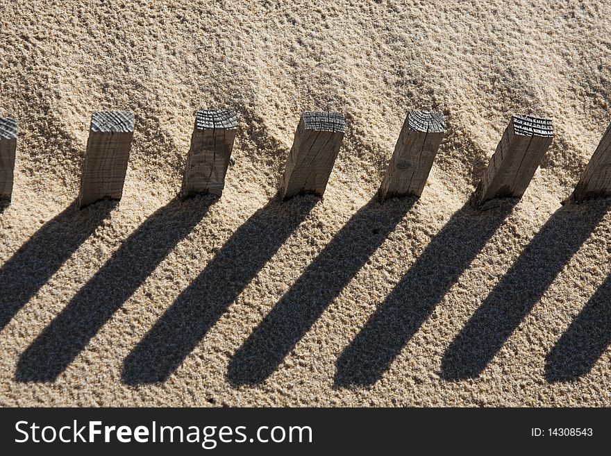 View of a section of a fence buried on the sand making a shadow. View of a section of a fence buried on the sand making a shadow.