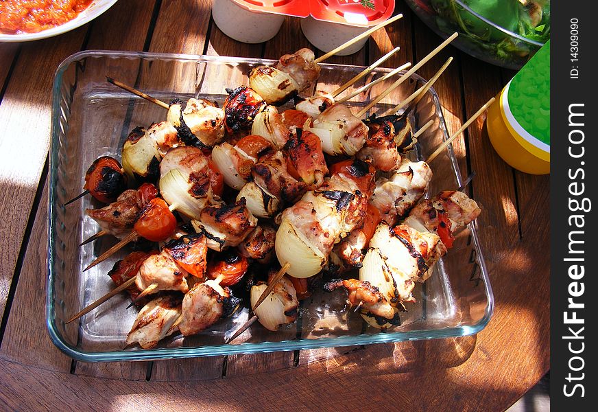 Barbecue sticks with meat, tomatoes and onions in a glass tray on the table. Barbecue sticks with meat, tomatoes and onions in a glass tray on the table