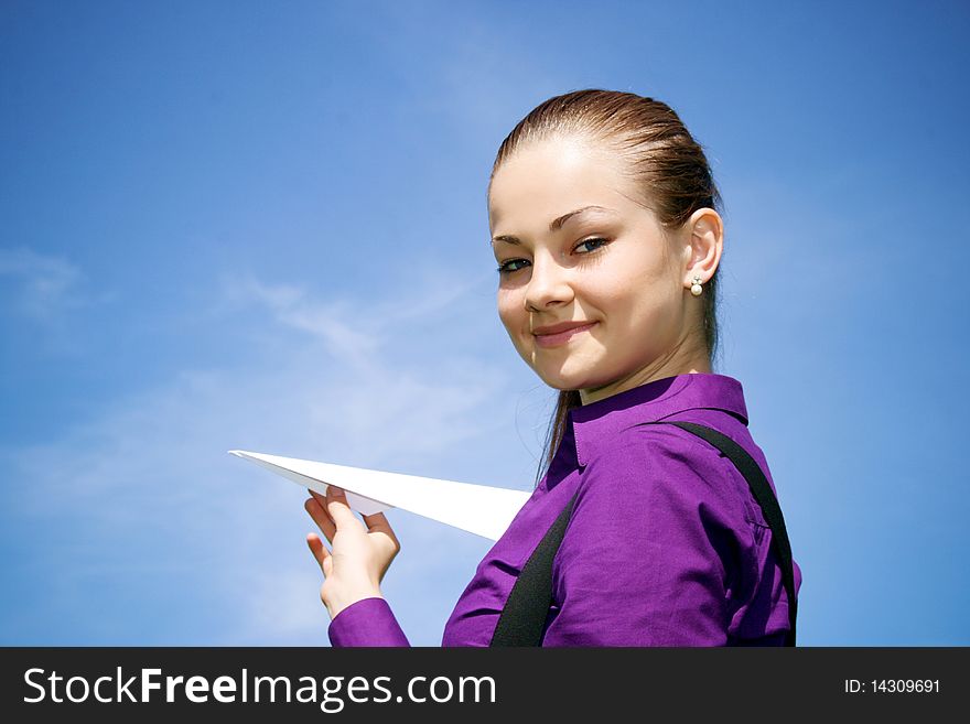 Young caucasian girl with paper plane in the hand against blue sky