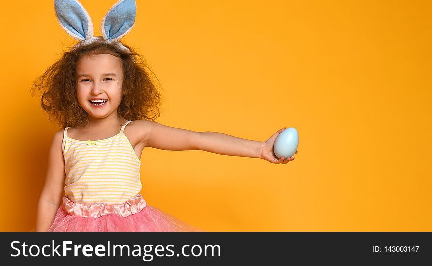 Cute little child girl wearing bunny ears on Easter day. Girl holding egg on yellow background