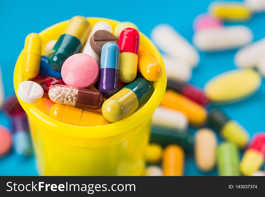 Many colored pills and capsules in yellow container on a blue background