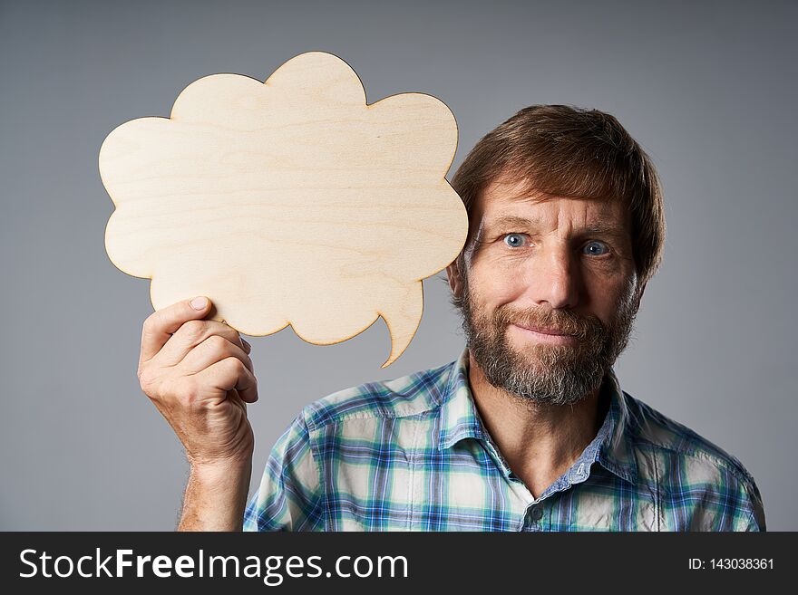 Mature man in checkered shirt holding speech bubble looking at camera, over grey studio background. Mature man in checkered shirt holding speech bubble looking at camera, over grey studio background