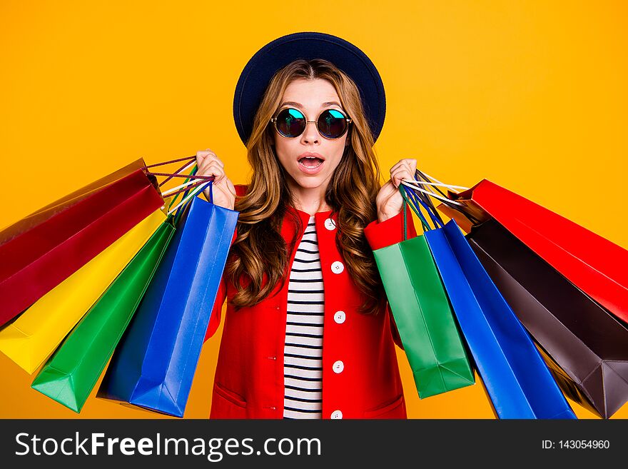 Portrait of shocked charming elegant adorable curly-haired lady in eyeglasses eyewear holding many colorful bags wearing fall modern outfit isolated over yellow background