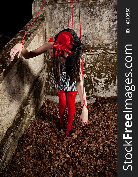 Beautiful girl wearing red hat and striped dress posing as a marionette (puppet on a string)