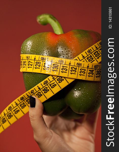 View of a woman's hand holding a bell pepper with measuring tape. View of a woman's hand holding a bell pepper with measuring tape.