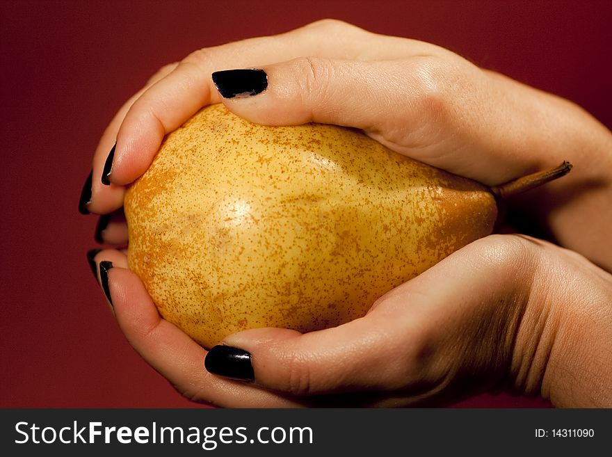 Close view of a woman hands holding a pear over a red background.