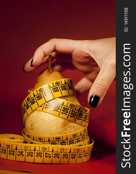 View of a woman's hand trying to grab a pear with measuring tape.