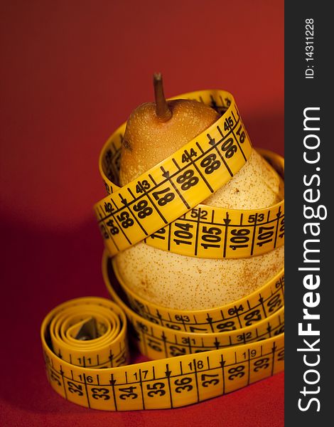 Close view of a pear with measuring tape over a red background.