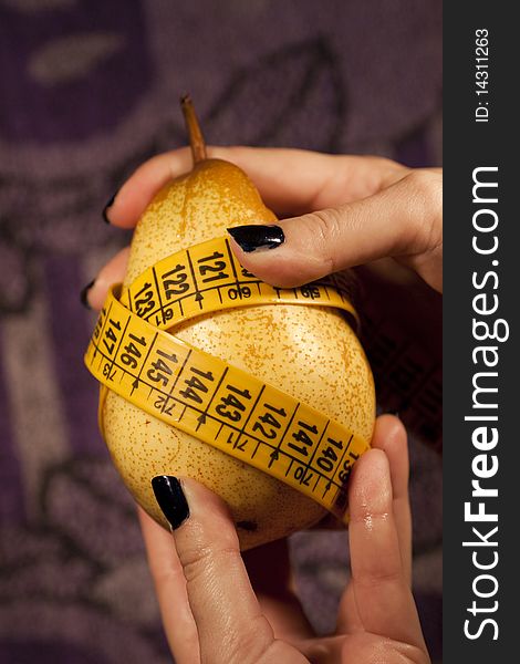 View of a woman's hand grabbing a pear with measuring tape.