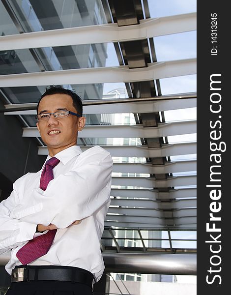A smiling young successful Asian businessman standing with his arms crossed below a skylight