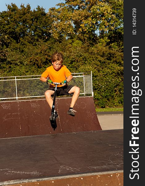 Child, boy is jumping with a scooter over a fun box in the skate parc and enjoying it. Child, boy is jumping with a scooter over a fun box in the skate parc and enjoying it