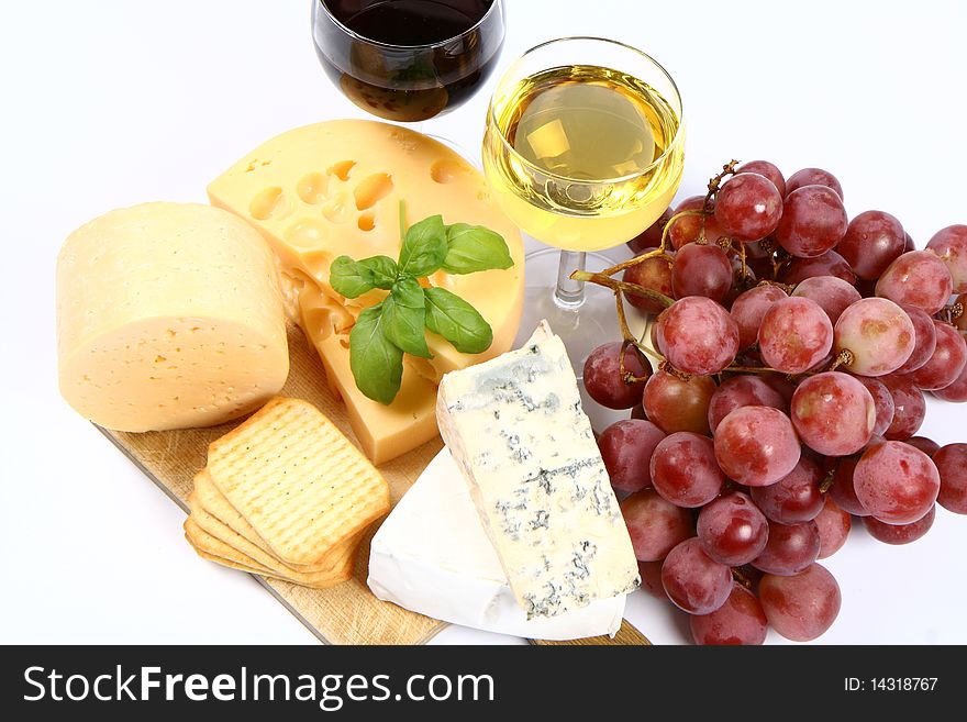 Various types of cheese (swiss, yellow, brie, blue cheese) with red and white wine, red grapes and crackers in close up on white background