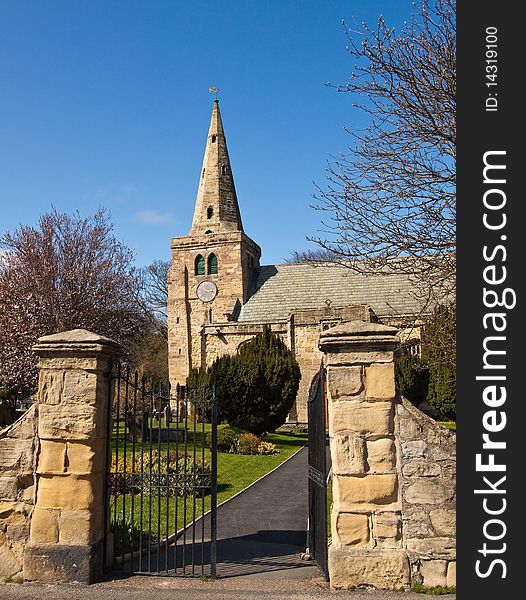 A small church with a leaning tower and spire. The gate leads the eye into the churchyard through the grounds to the church. A small church with a leaning tower and spire. The gate leads the eye into the churchyard through the grounds to the church.