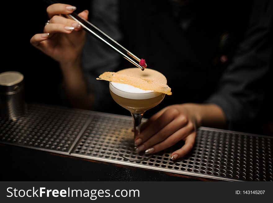 Professional bartender girl adding to a delicious cocktail decor of the little rose bud