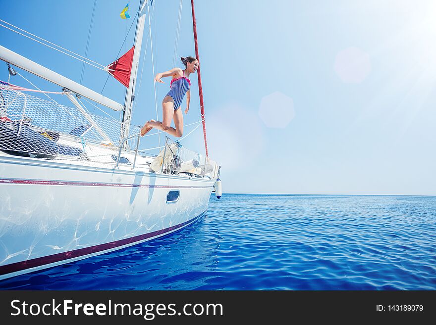 Girl jump in sea of sailing yacht on summer cruise. Travel adventure, yachting with child on vacation.