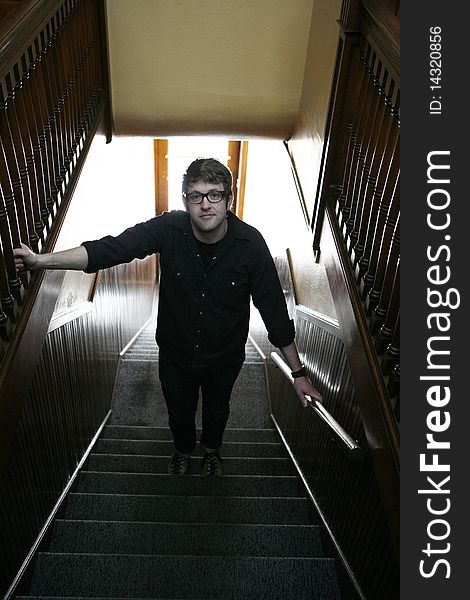 Young college age man wearing glasses standing in stairwell looking at camera seriously. Young college age man wearing glasses standing in stairwell looking at camera seriously