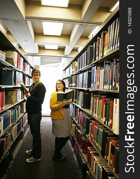 College age students reading books in library whispering to each other in library. College age students reading books in library whispering to each other in library