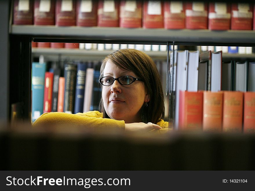 Female student with glasses in library looking through shelves