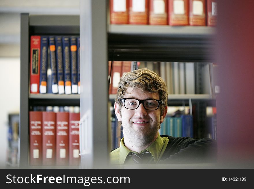 Male student with glasses in library smiling into camera