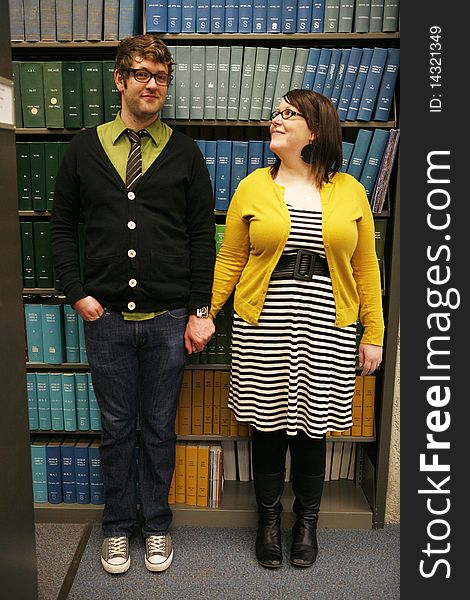 College age students holding hands standing in front of books in library. College age students holding hands standing in front of books in library