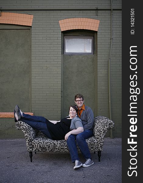Young couple sitting together on pattern couch outside on the city street in front of building. Young couple sitting together on pattern couch outside on the city street in front of building