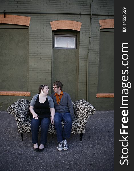 Young couple sitting together on pattern couch outside on the city street in front of building. Young couple sitting together on pattern couch outside on the city street in front of building