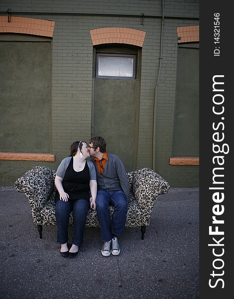 Young couple sitting together on pattern couch outside on the city street in front of building. Young couple sitting together on pattern couch outside on the city street in front of building