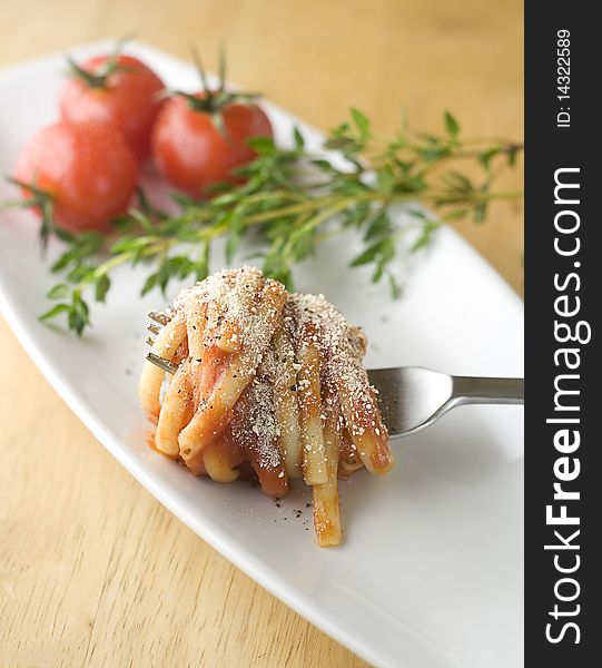 Linguine in tomato sauce and parmesan, coiled around fork on tasting plate with fresh herbs and cherry tomatos in background. Linguine in tomato sauce and parmesan, coiled around fork on tasting plate with fresh herbs and cherry tomatos in background.