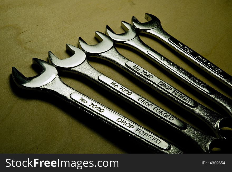 A collection of silver metal wrenches in a row on a wood background. A collection of silver metal wrenches in a row on a wood background.