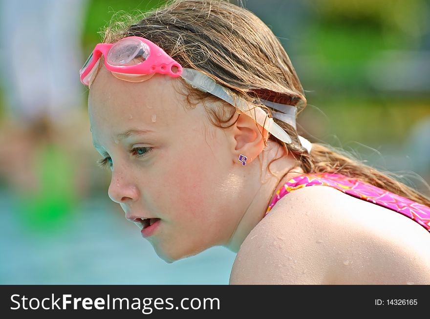 A young girl with goggles on her head sitting at the water. A young girl with goggles on her head sitting at the water.